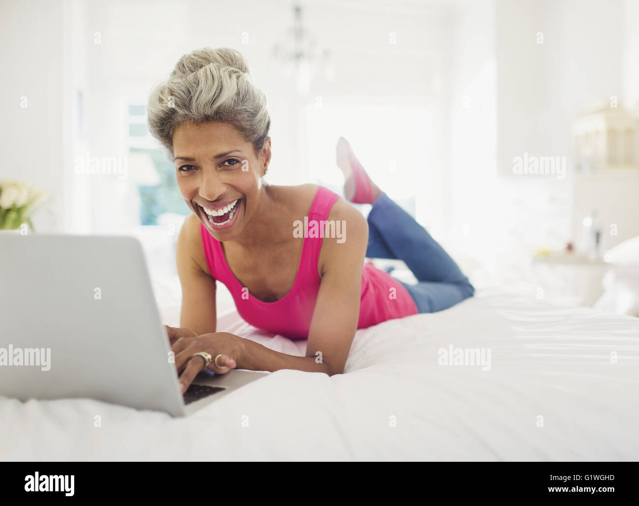 Portrait laughing mature woman using laptop on bed Stock Photo