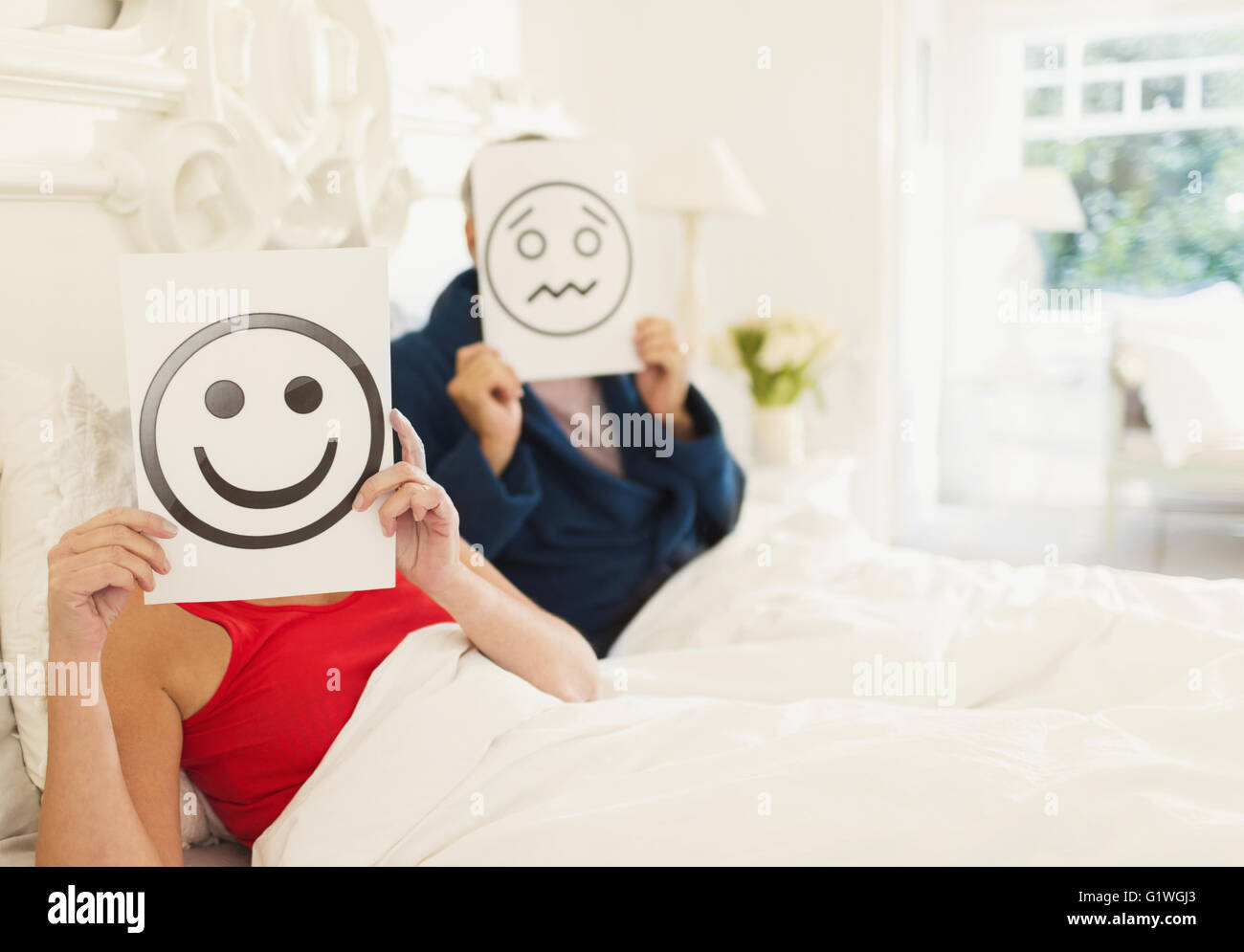 Portrait of couples holding smiling face and frowning face printouts in bed Stock Photo