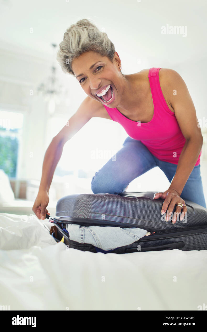 Portrait enthusiastic mature woman closing suitcase on bed Stock Photo