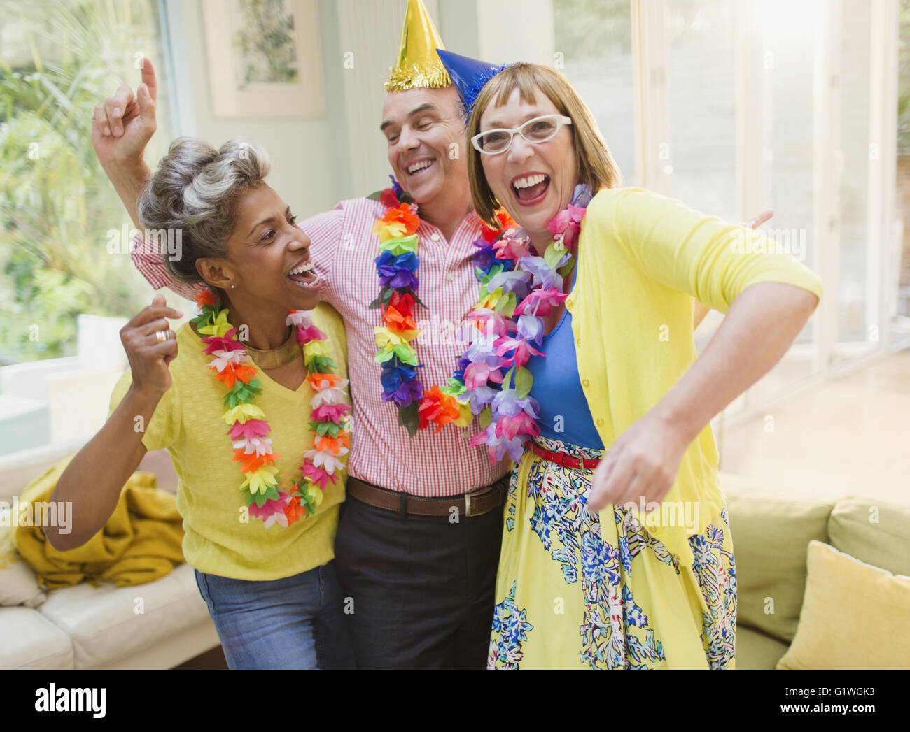 Playful mature adults dancing with leis in living room Stock Photo