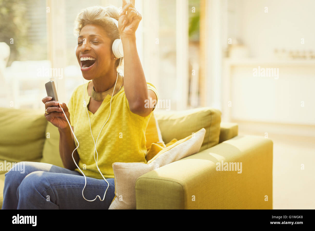 Playful mature woman listening to headphones with MP3 player in living room Stock Photo