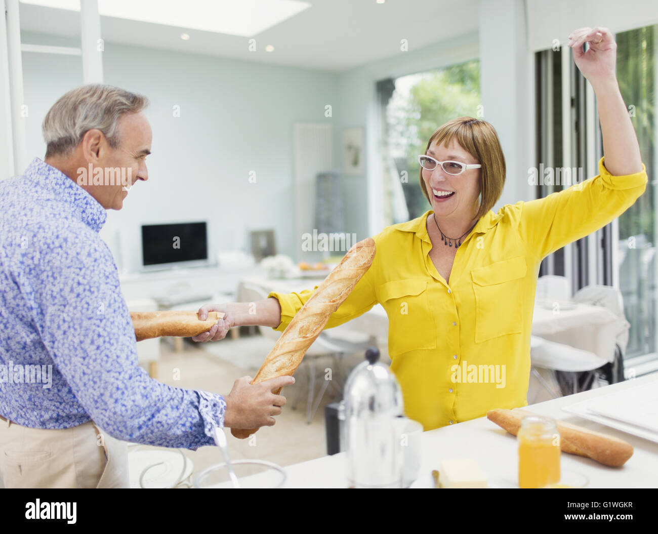 Playful mature couple sword fighting with baguettes in kitchen Stock Photo