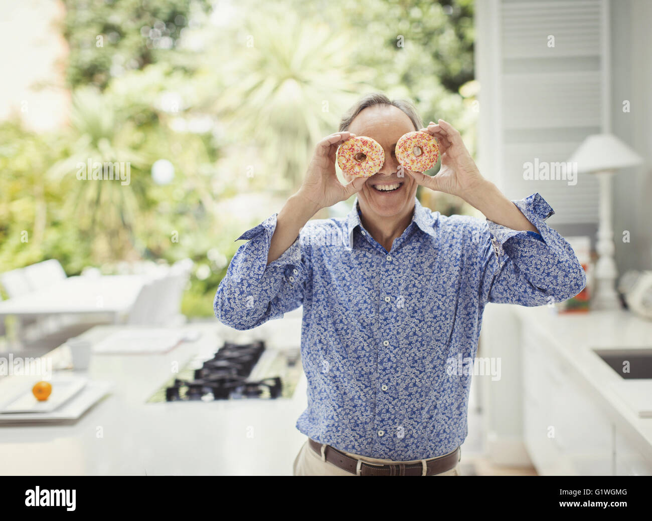 Portrait playful mature man covering eyes with donuts Stock Photo