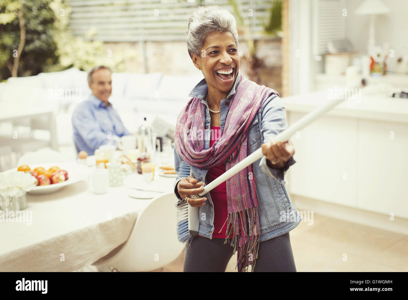 Portrait playful mature woman playing air guitar with stick in kitchen Stock Photo