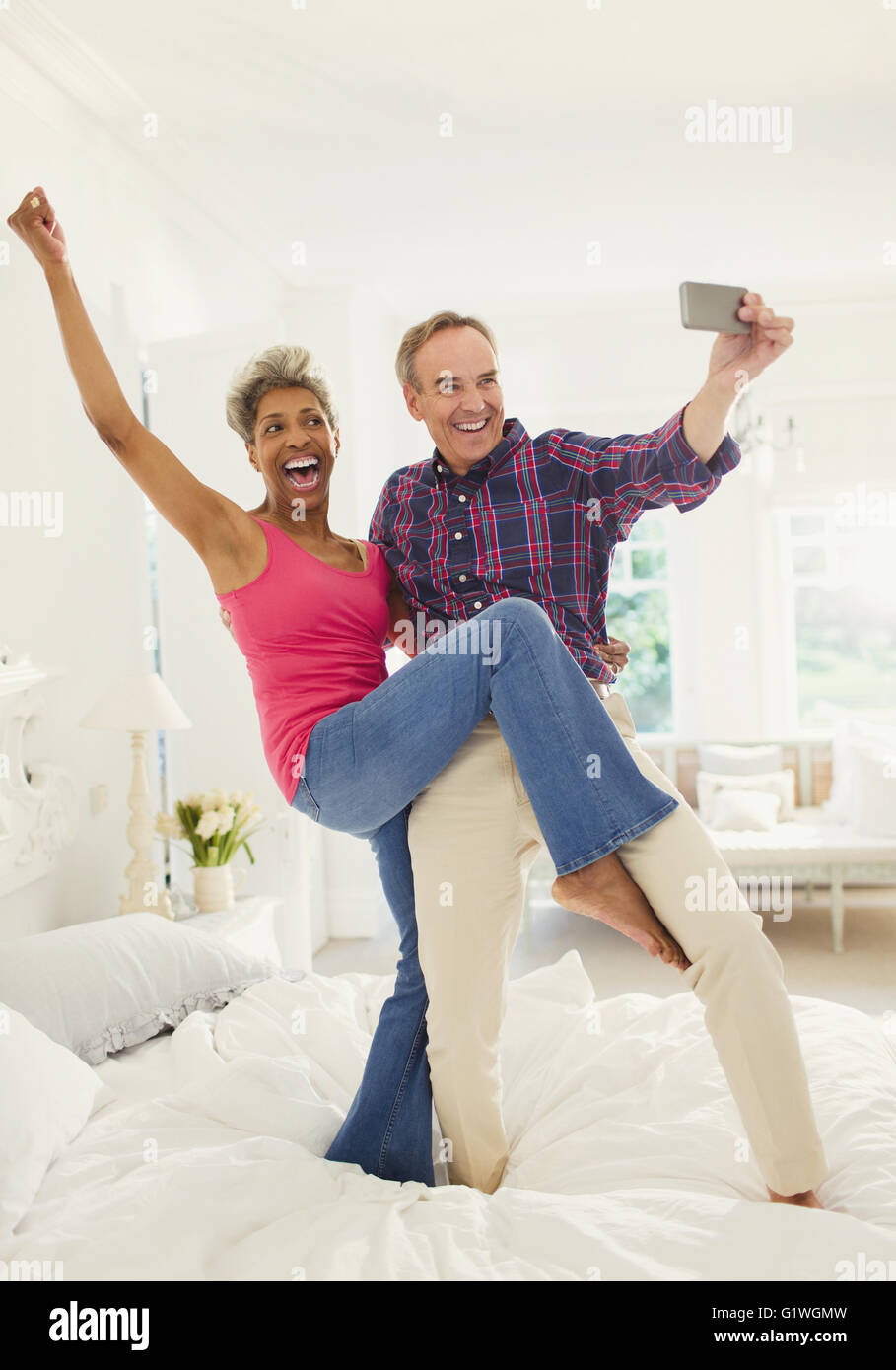 Playful mature couple taking selfie standing on bed Stock Photo