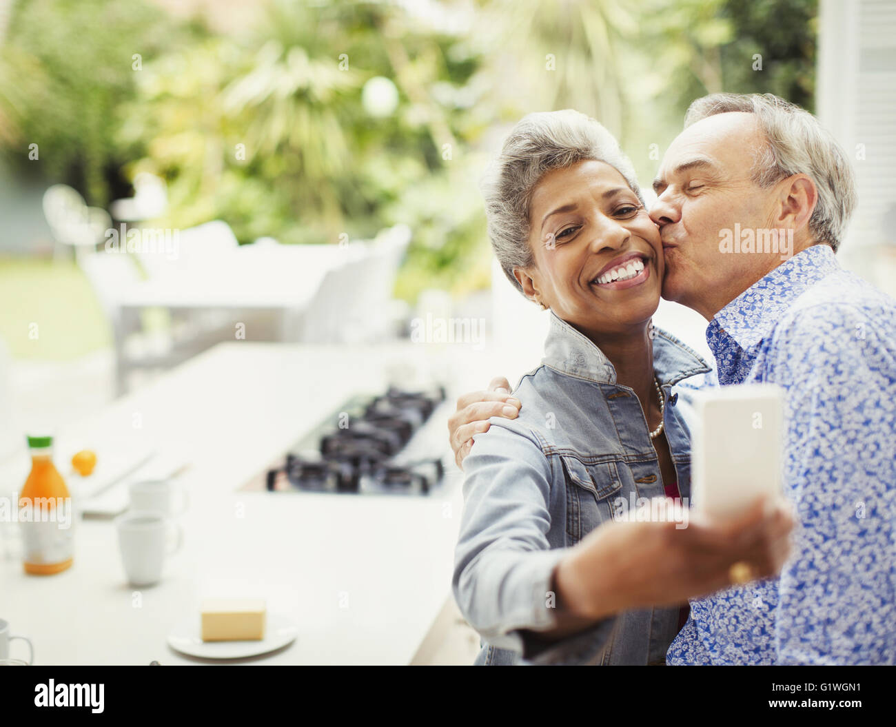 Affectionate mature couple kissing taking selfie in kitchen Stock Photo