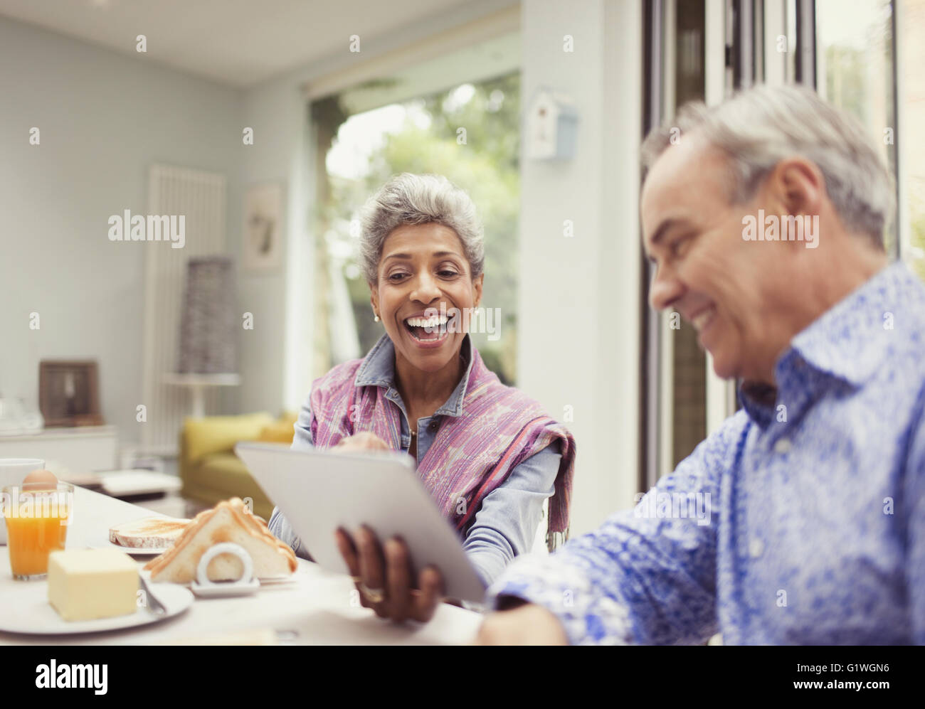 Mature couple laughing and using digital tablet at breakfast table Stock Photo