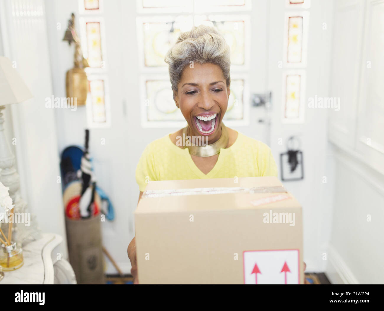 Enthusiastic mature woman receiving package in foyer Stock Photo