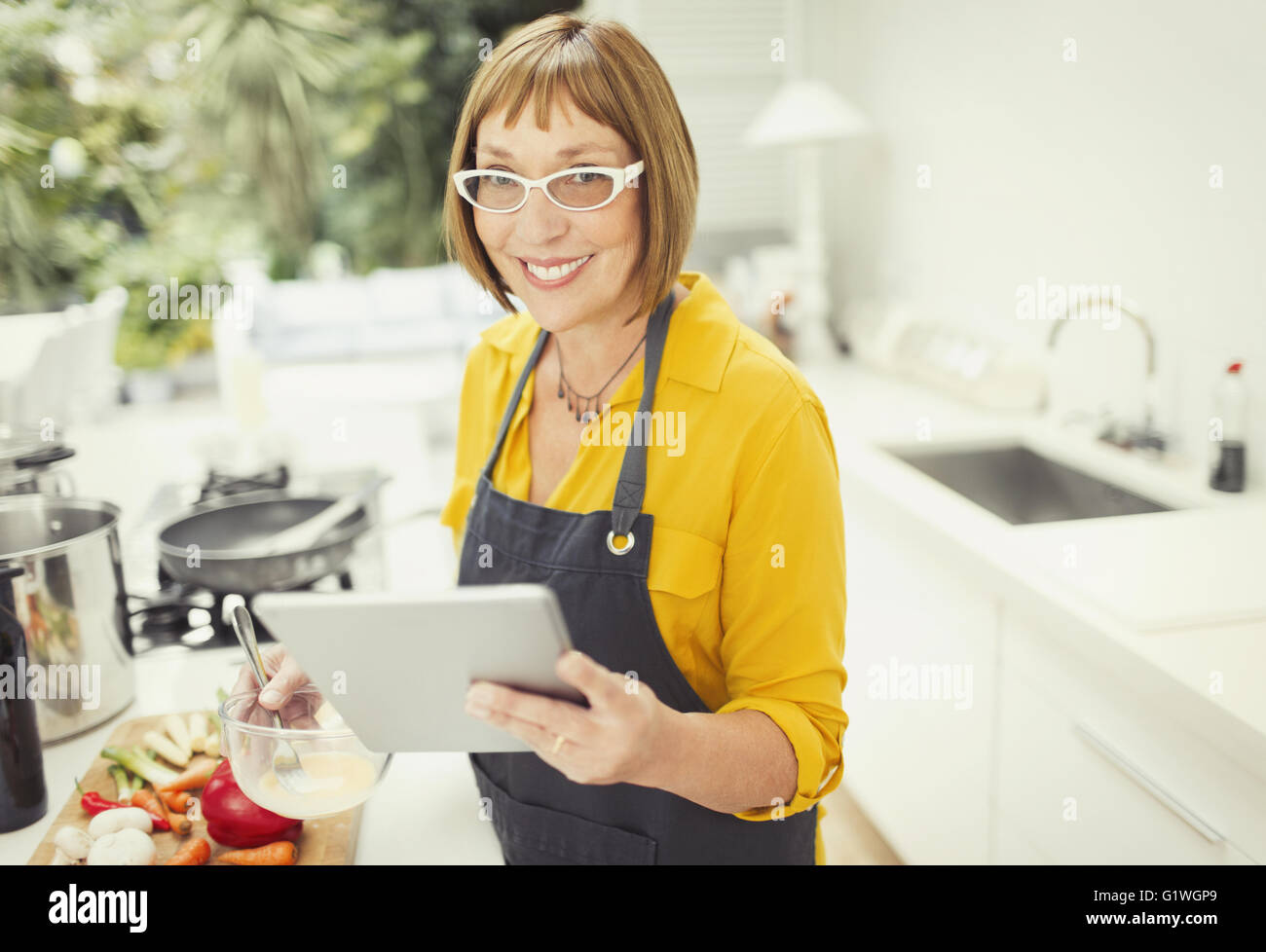 Portrait smiling mature woman with digital tablet cooking in kitchen Stock Photo