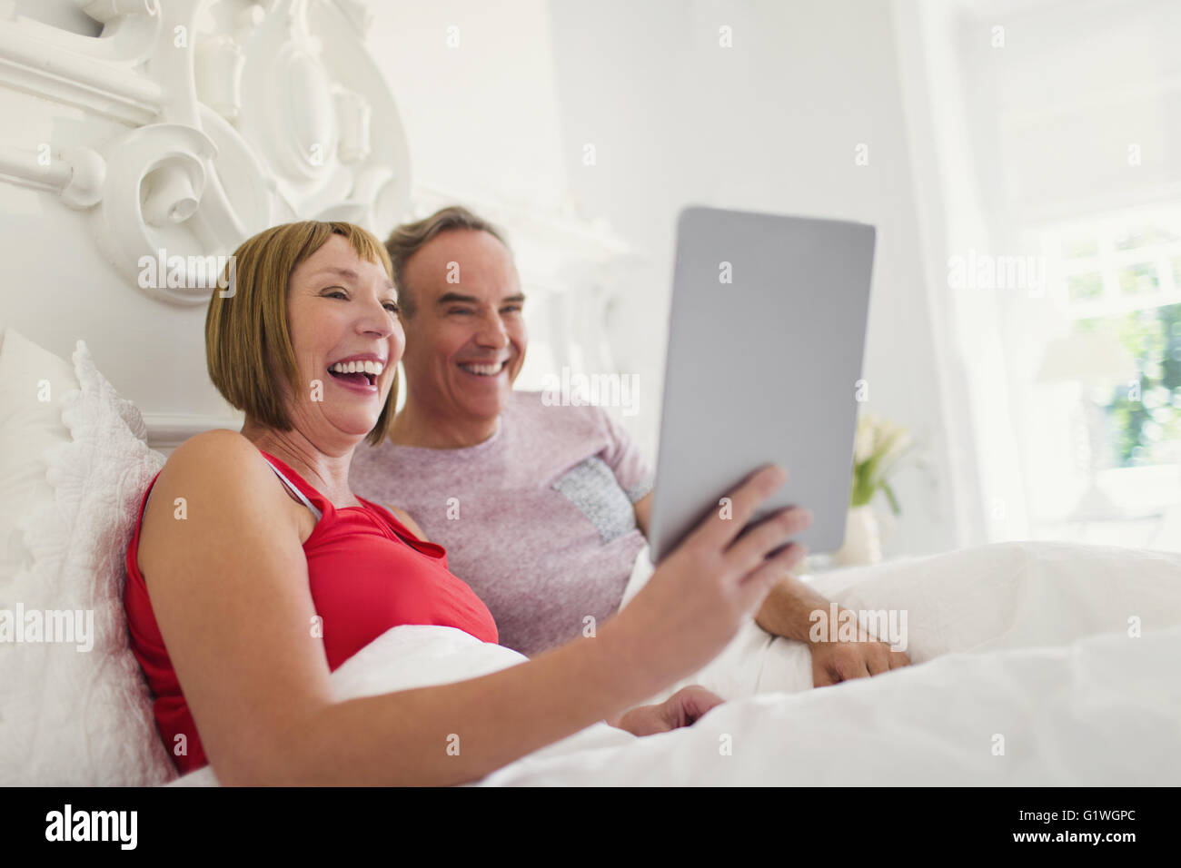 Laughing mature couple using digital tablet in bed Stock Photo