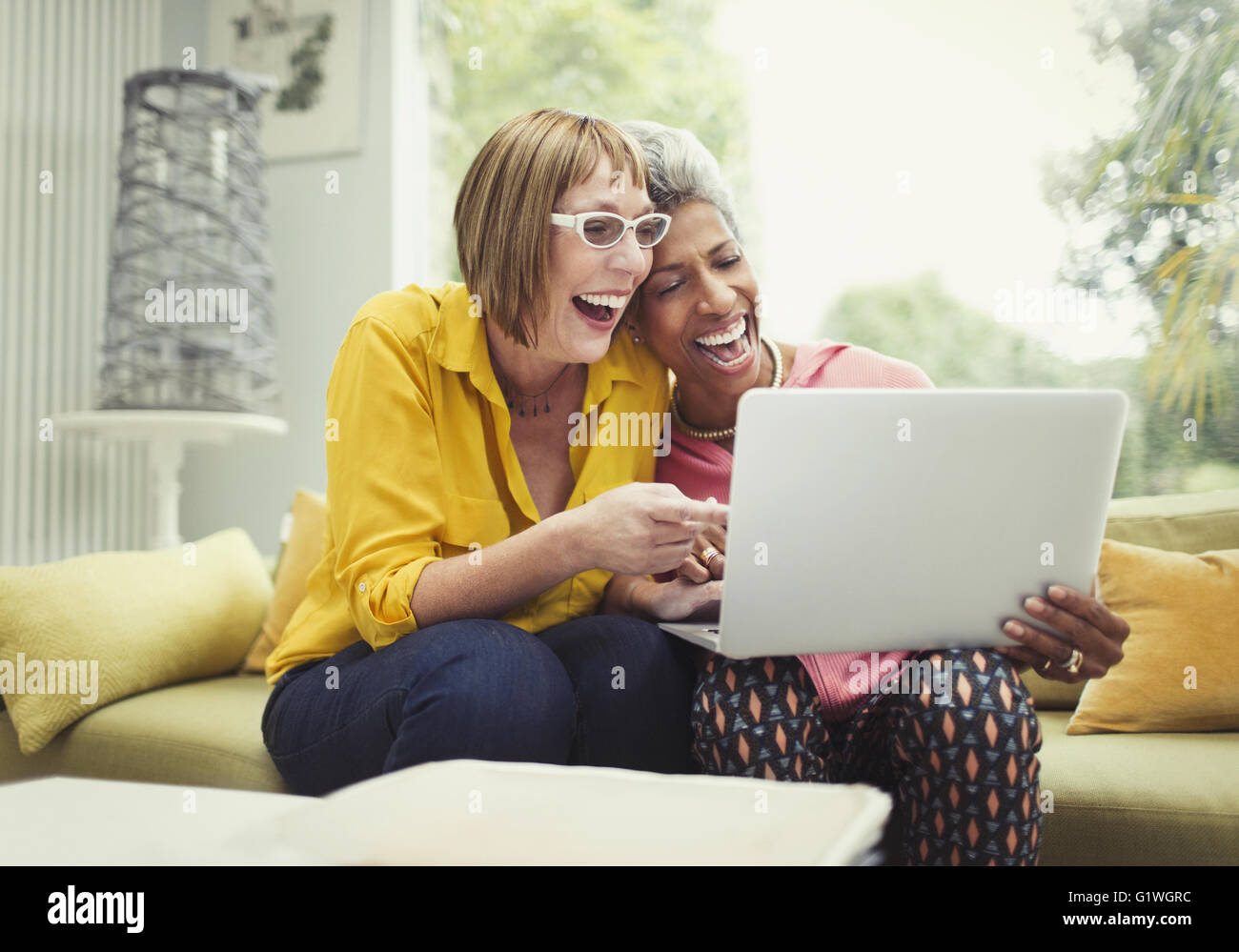 Laughing mature women sharing laptop on living room sofa Stock Photo