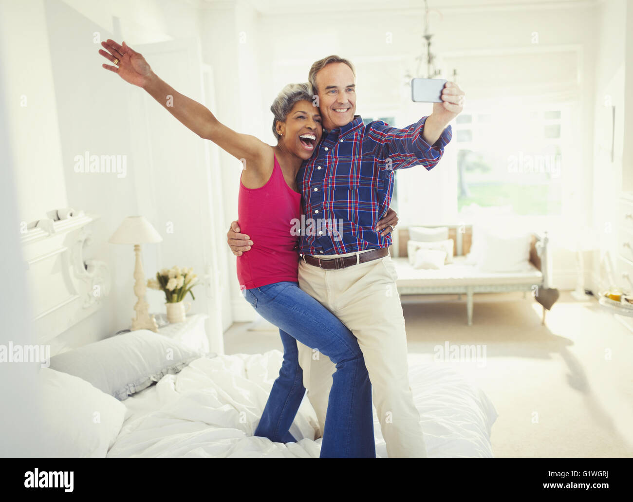 Playful mature couple taking selfie standing on bed Stock Photo