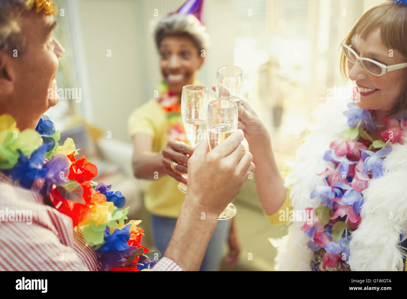 Playful mature friends in feather boas and leis toasting champagne flutes Stock Photo