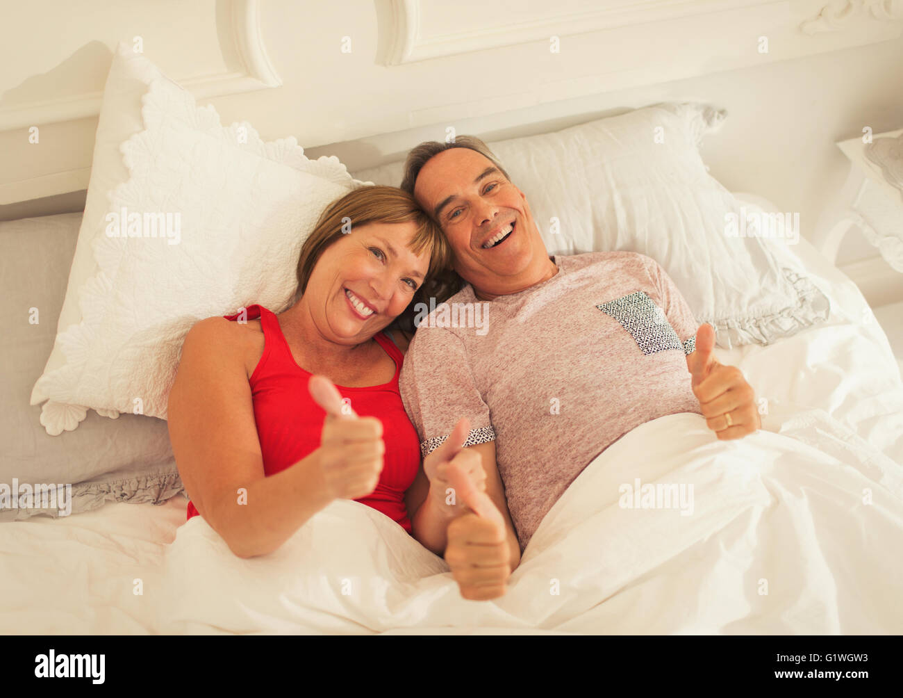 Portrait playful mature couple gesturing thumbs-up in bed Stock Photo