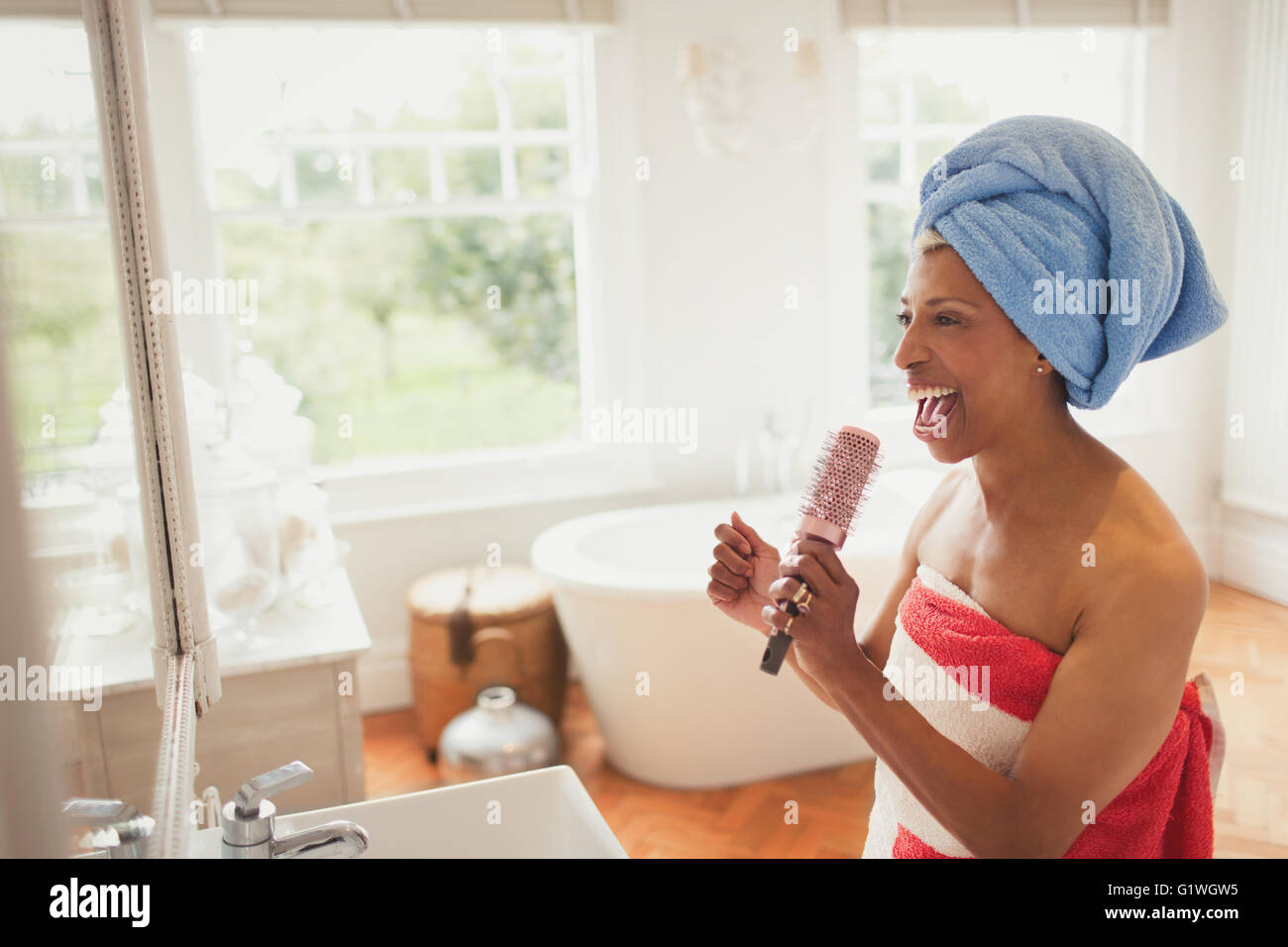 Playful mature woman singing into hairbrush in bathroom Stock Photo