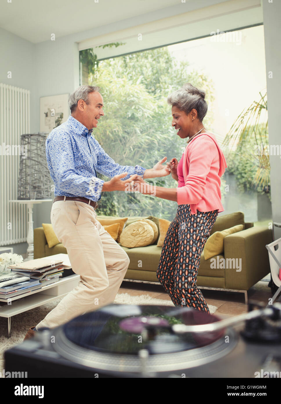 Playful mature couple dancing behind record player in living room Stock Photo