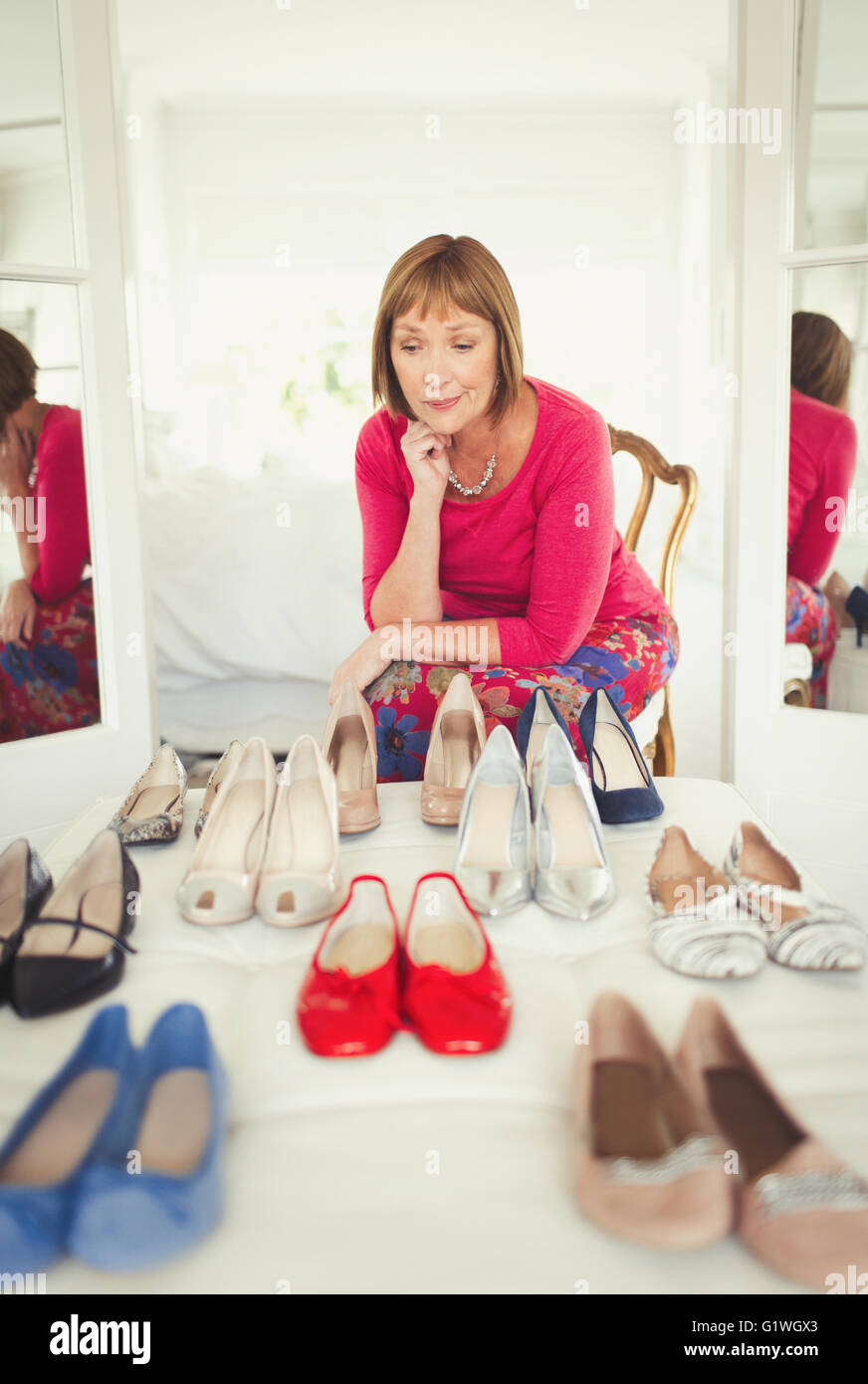 Indecisive mature woman deciding which shoes to wear in closet Stock Photo