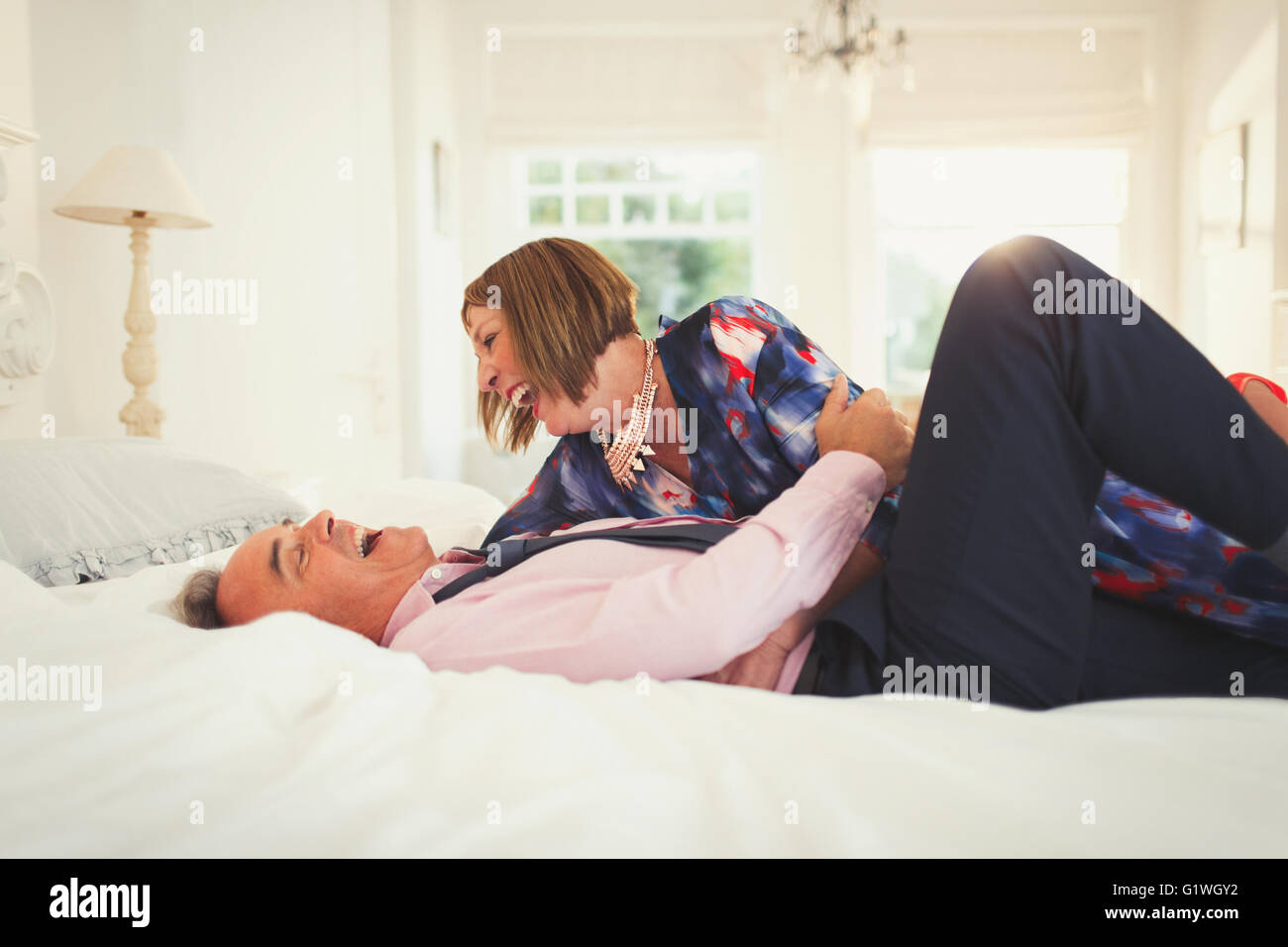 Well-dressed mature couple laughing on bed Stock Photo