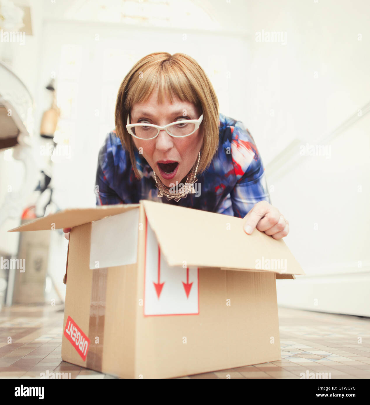 Surprised mature woman opening package on foyer floor Stock Photo