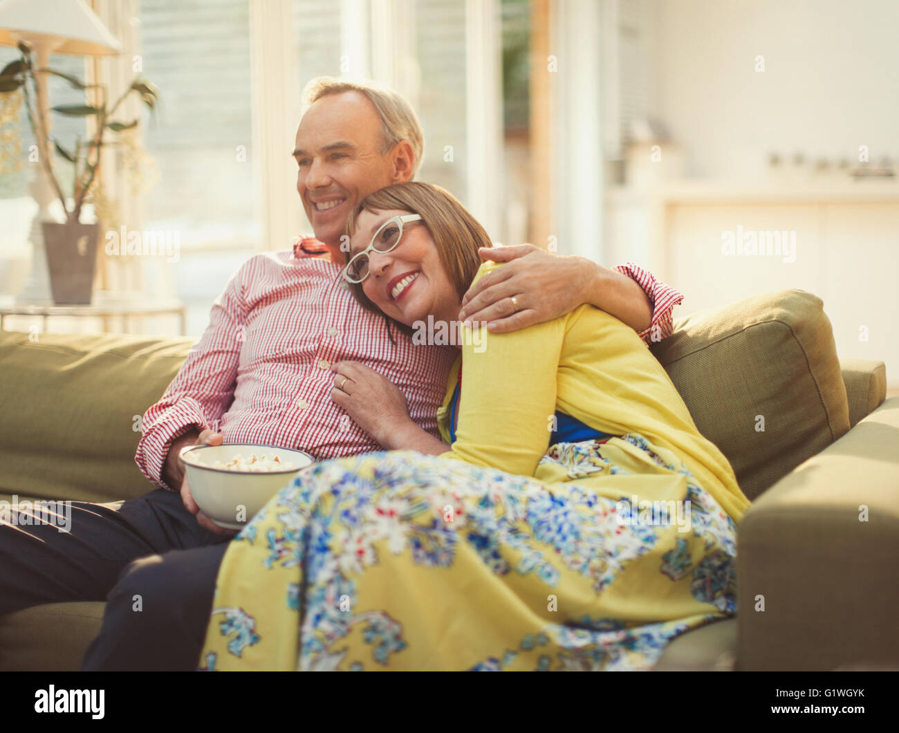Affectionate mature couple watching TV and eating popcorn on living room sofa Stock Photo