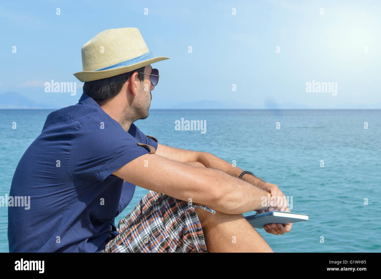 Man in blue shirt sitting on the dock holding a book Stock Photo