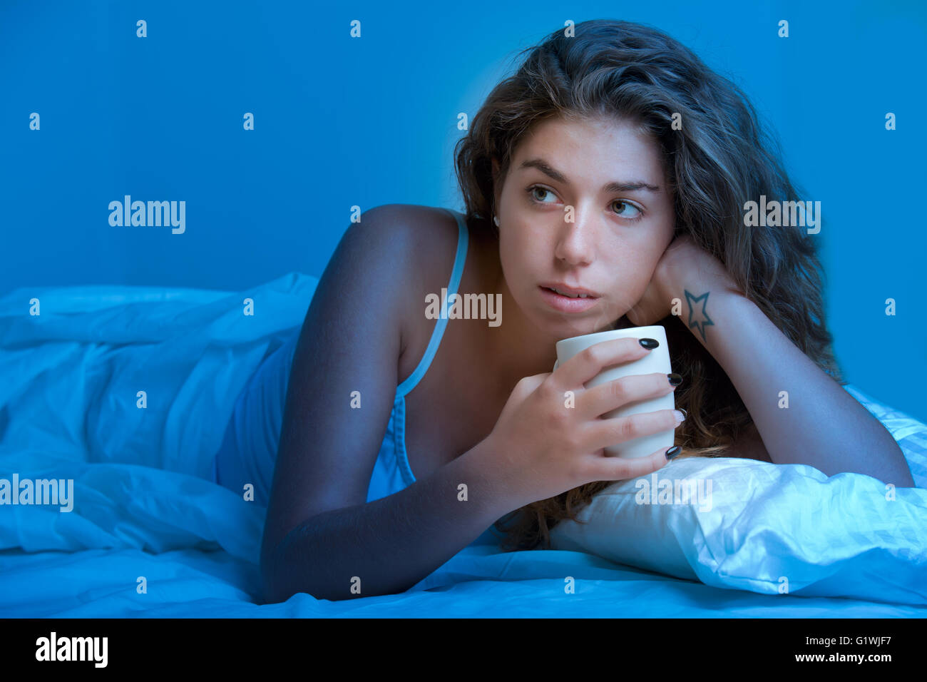 Woman lying in a bed, drinking a hot coffee and relaxing in the dark Stock Photo