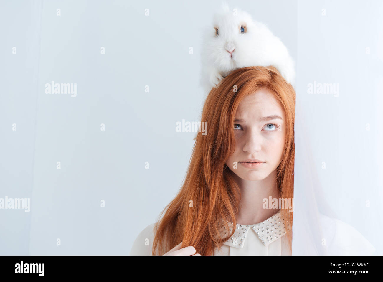 Portrait of a beautiful redhead woman posing with rabbit on her head ...