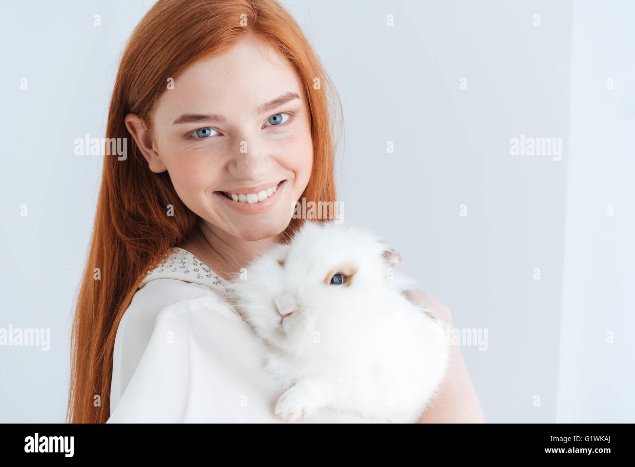 Cheerful redhead woman posing with rabbit isolated on a white ...