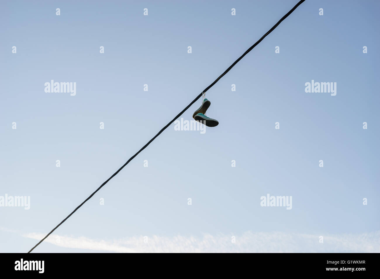 Old pair of sneakers dangling on power line cable against blue sky, life change concept Stock Photo