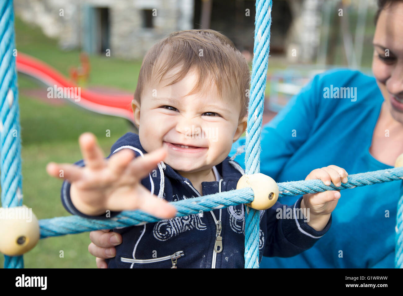 Mother with one year old daughter pulling her arm while looking at camera Stock Photo
