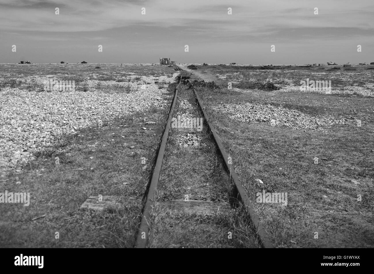 Dungeness beach with rail tracks down to the English Channel and disused ruined buildings in the distance in black & white Stock Photo