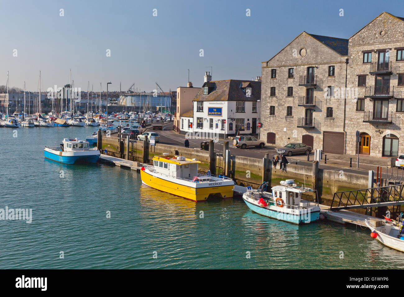 Two colourful fishing boats are moored alongside an old warehouse in Weymouth harbour, Dorset, England, UK Stock Photo