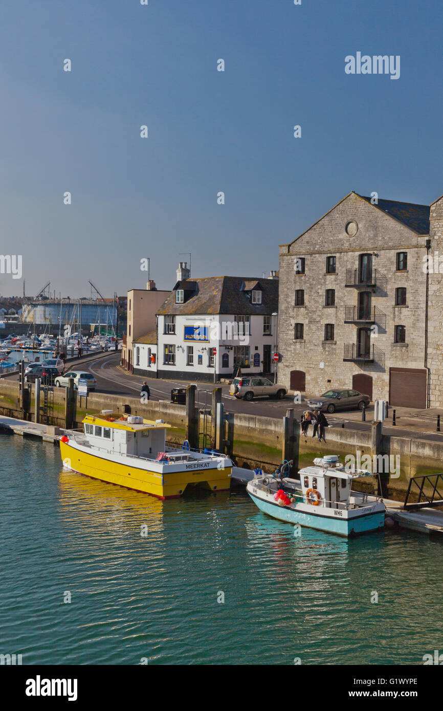 Two colourful fishing boats are moored alongside an old warehouse in Weymouth harbour, Dorset, England, UK Stock Photo