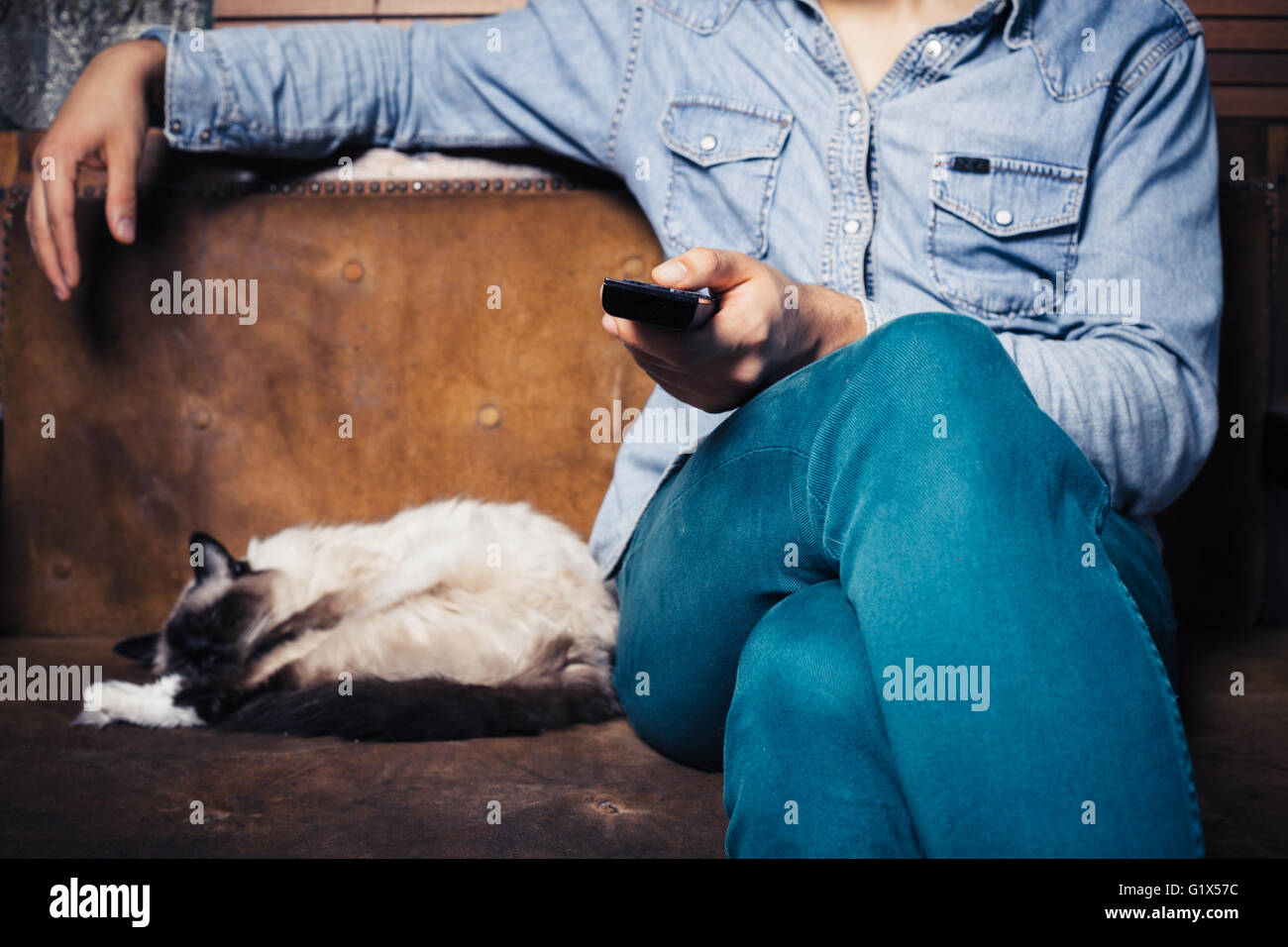 A young man is sitting on a sofa with a cat and is watching television Stock Photo