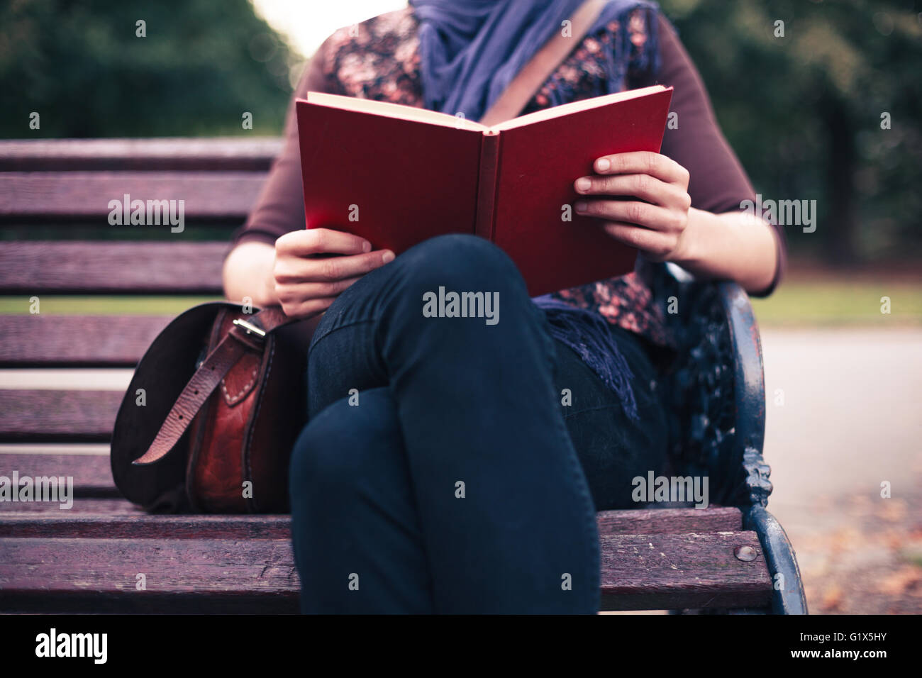 A young woman is sitting on a park bench and is reading a book Stock ...