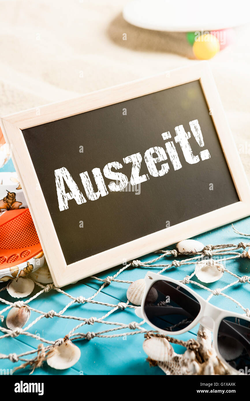 Beach with holiday gear and a board with the word Auszeit Stock Photo