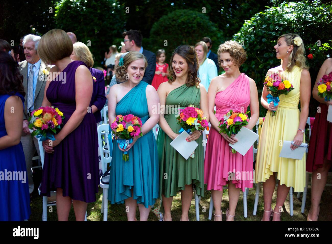 Bridesmaids waiting for bride to arrive at outdoor wedding ceremony whilst wearing bright coloured dresses. Stock Photo