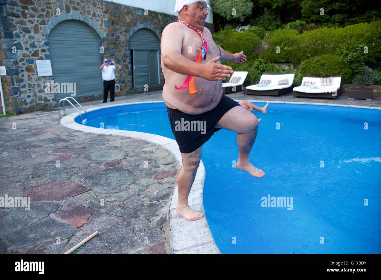 Overweight adult male jumping into swimming pool during a party. Stock Photo