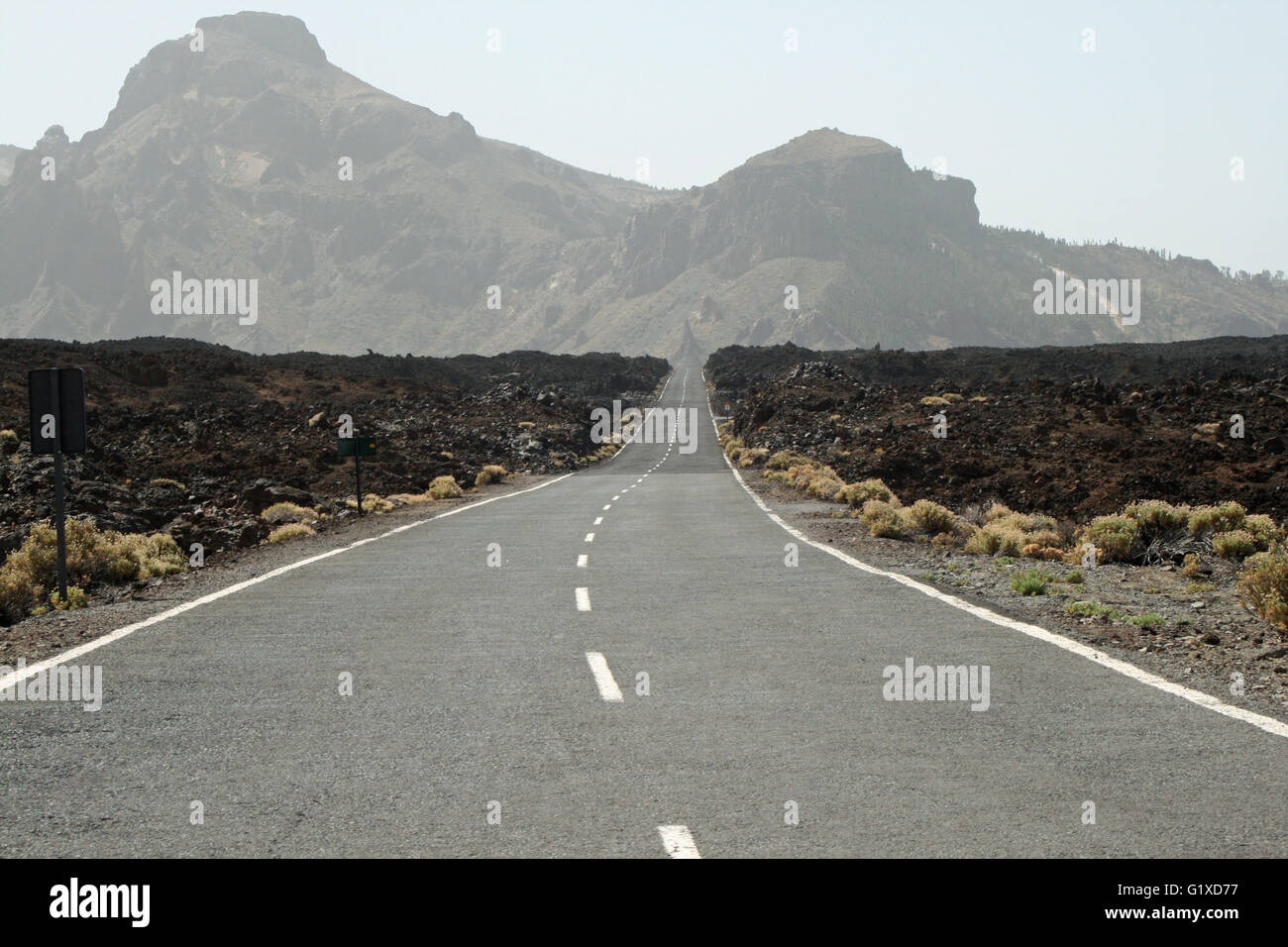 Road in Tenerife with mountains in background and scrub to either side Stock Photo