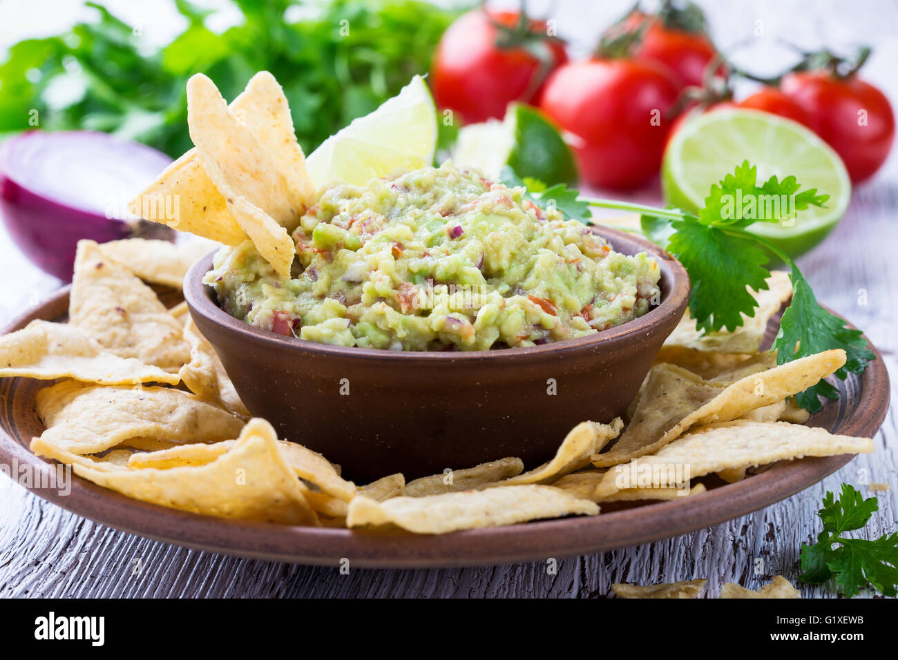 Homemade guacamole sauce and corn chips in ceramic bowl on wooden table, Mexican food Stock Photo