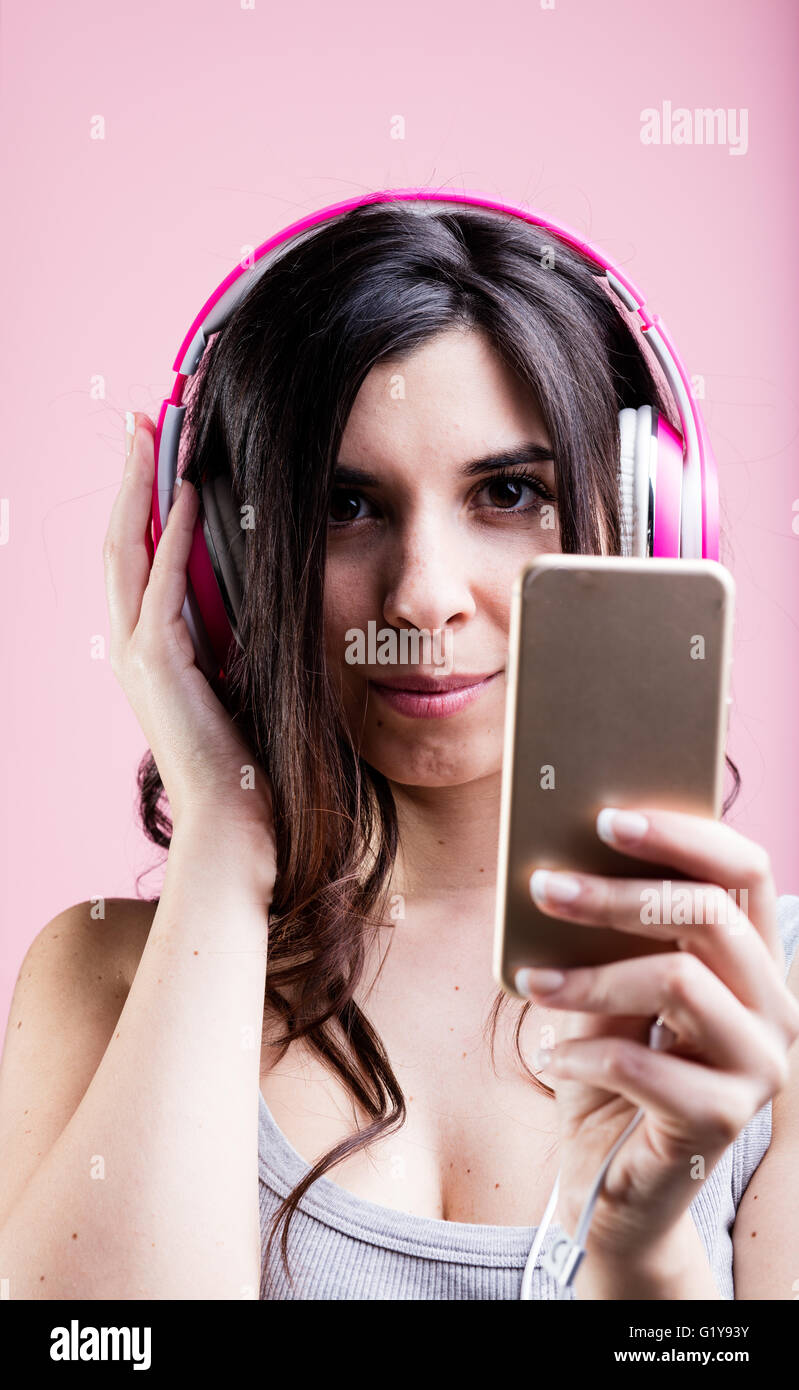 woman listening to music using a smartphone and her pink headphones: portrait on pink background Stock Photo