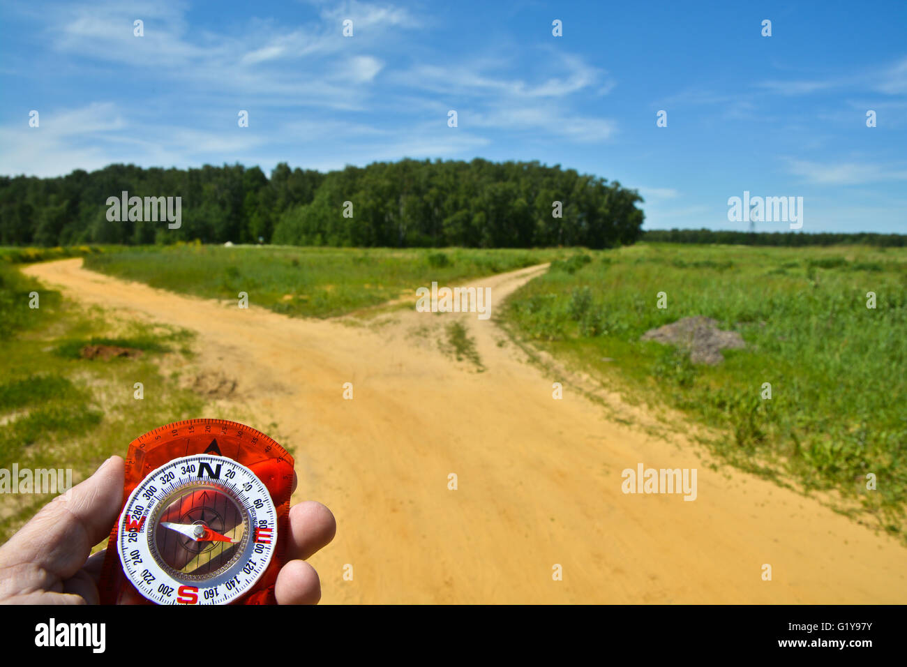 With the compass before the fork. The magnetic compass in the hand of a man to a fork in the road. Stock Photo