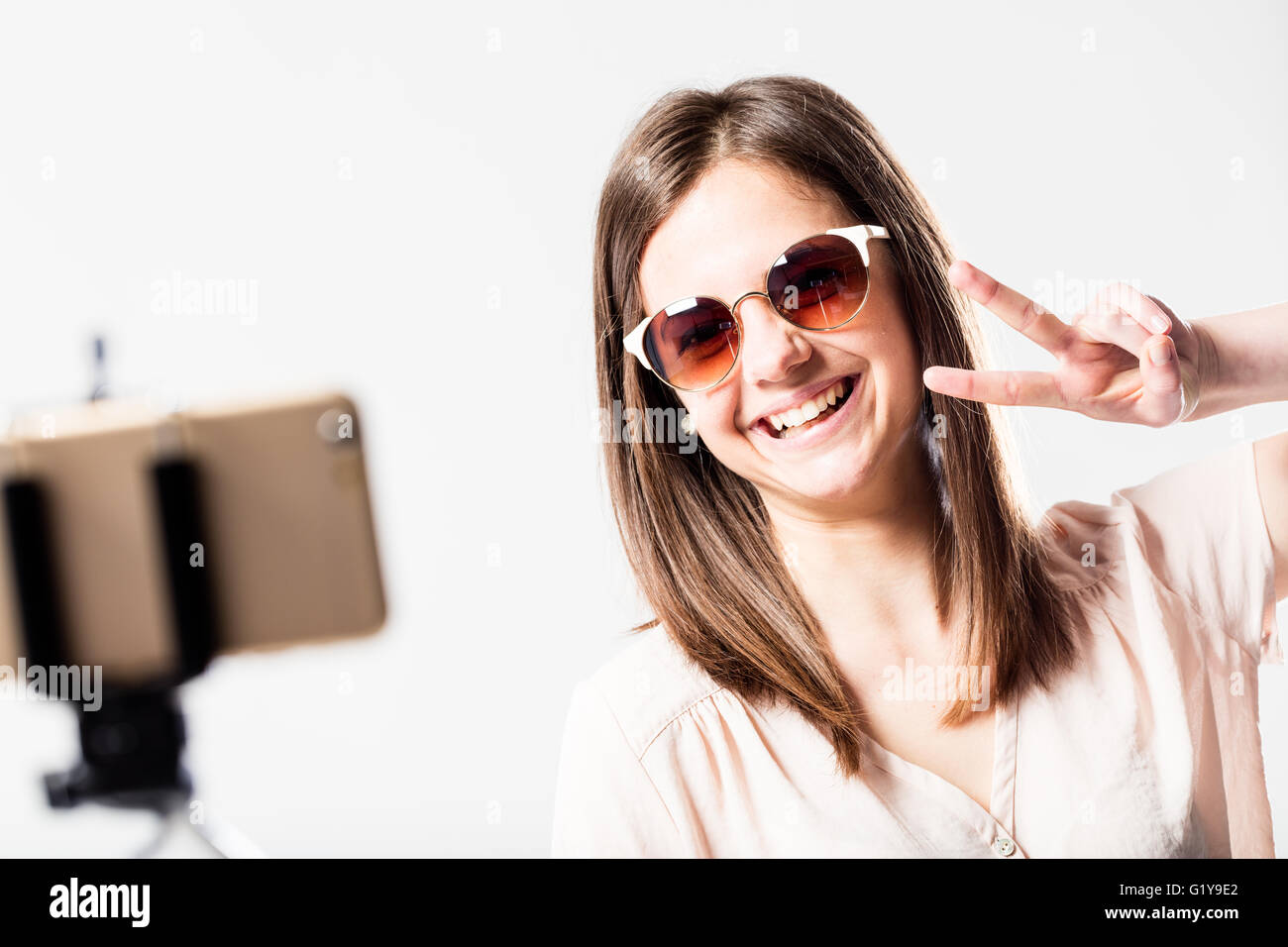 happy woman taking herself a selfie with his smartphone and a selfie stick with the victory sign Stock Photo
