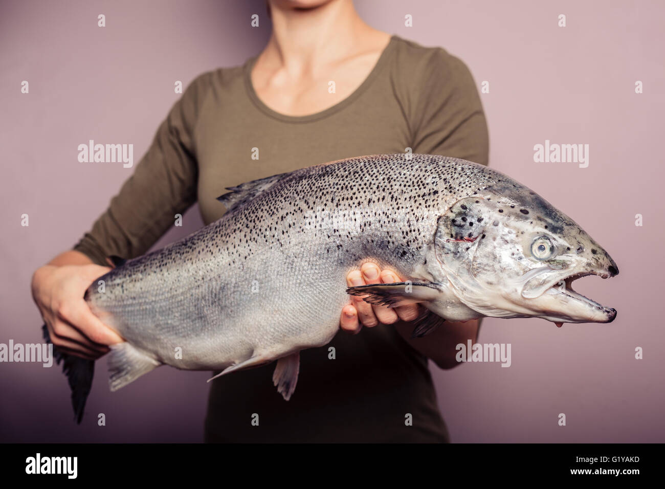A young woman is posing with a large atlantic salmon in her hands Stock Photo