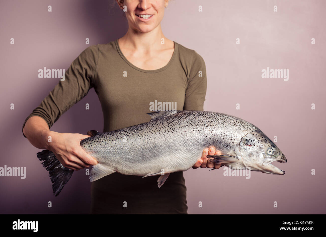 A young woman is posing with a large atlantic salmon in her hands Stock Photo