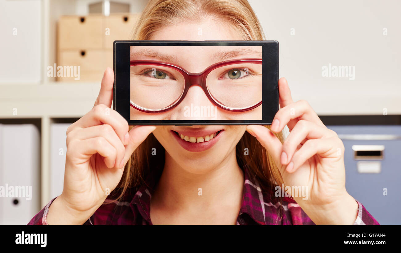 Face of a woman with glasses on a smartphone in front of the head of a woman at an office Stock Photo