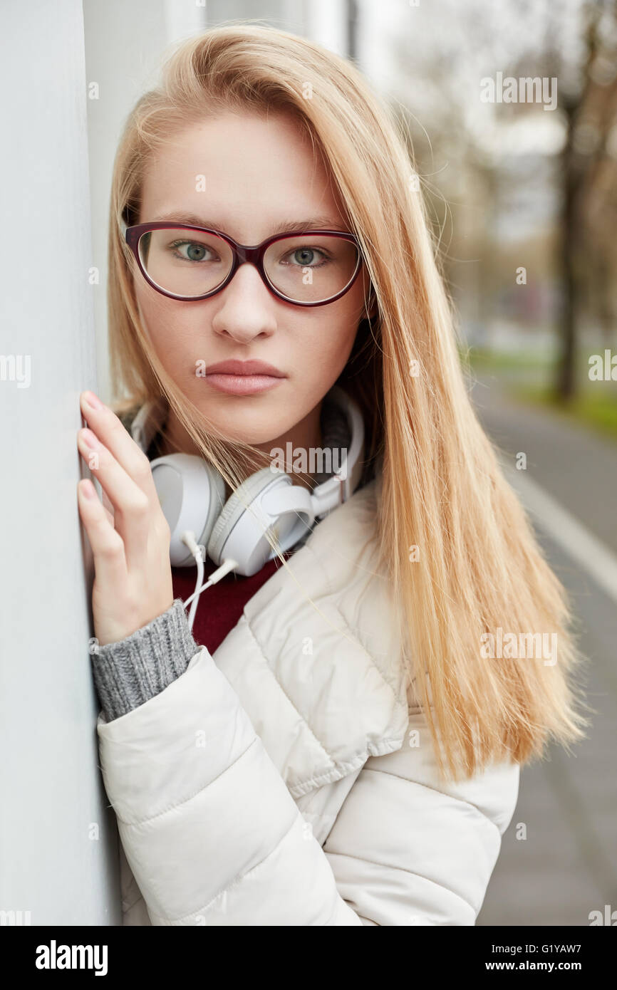 Young blond woman with headphones standing outside looking serious Stock Photo
