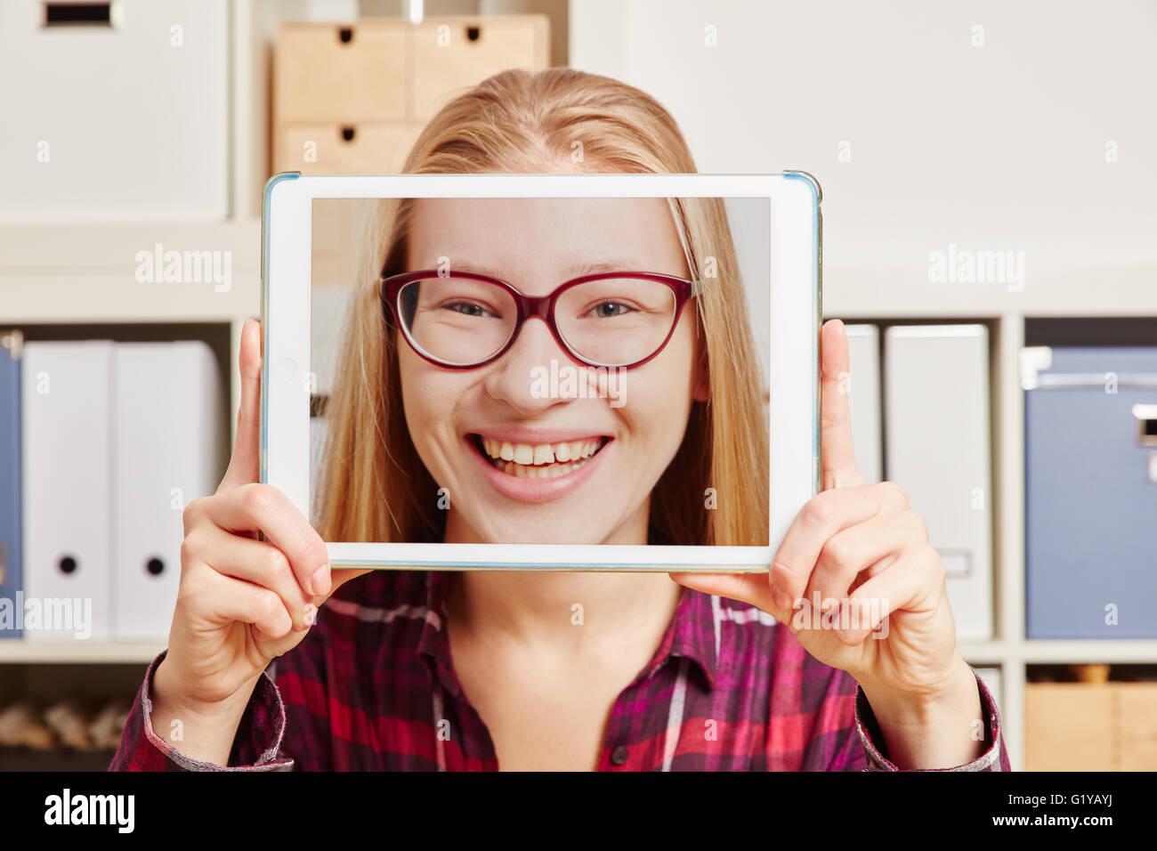 A woman holds a tablet in front of her with a smiling face in it Stock Photo