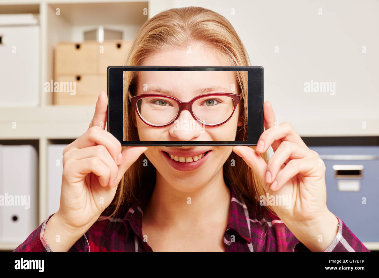 Young smiling woman holds a smartphone with her face in front of ther head Stock Photo