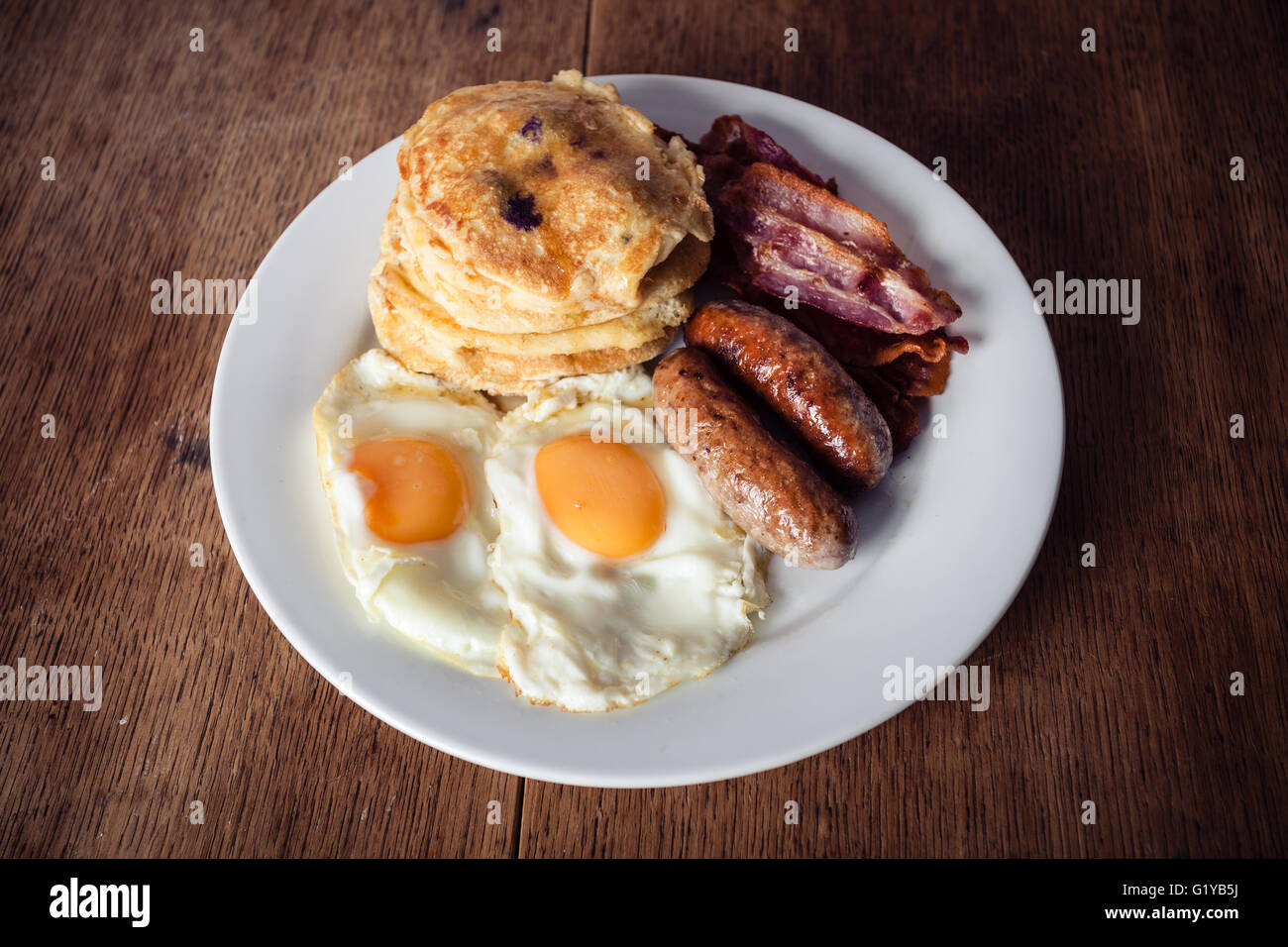 A breakfast with short stack of pancakes, bacon, eggs and sausage Stock